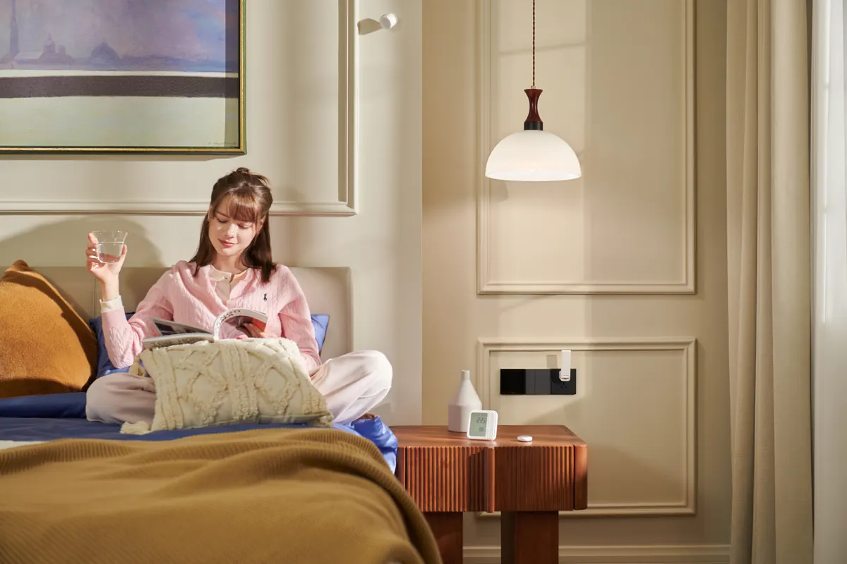 Person reading in bed in a bedroom with an Aqara Presence Sensor FP300 on the wall