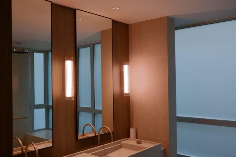 Bathroom vanity with tall mirrors, timber panels and ribbed wall sconces at The Light in Cairnhill.