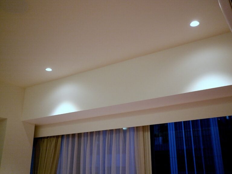 Living-room ceiling with a lit cove above the curtains and two recessed downlights.