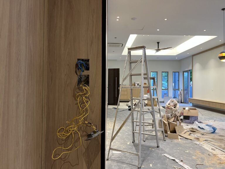 Switch wiring hanging from a timber wall panel beside a ladder in a home under renovation