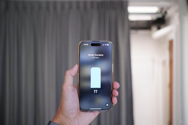 A hand holding a phone showing the smart curtain controls, with the curtains behind